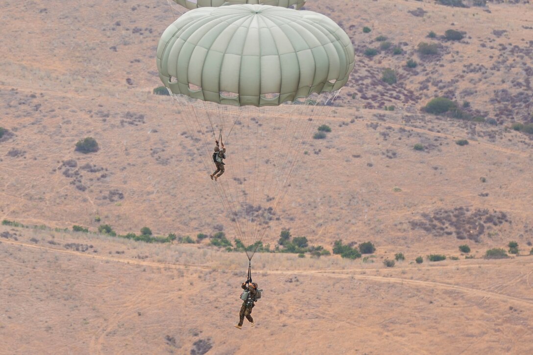 Two marines descend in the sky wearing parachutes.