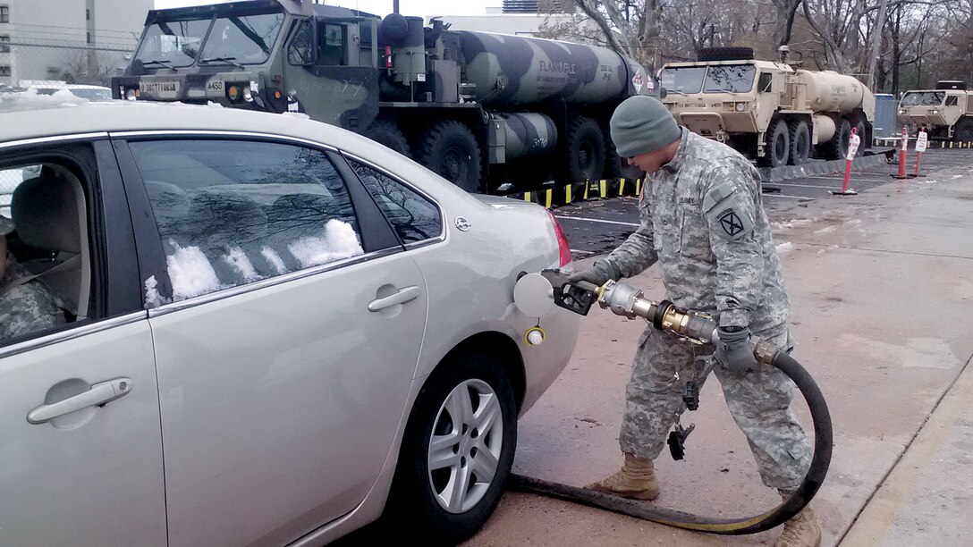 Man in camo uniform pumps fuel into a car.
