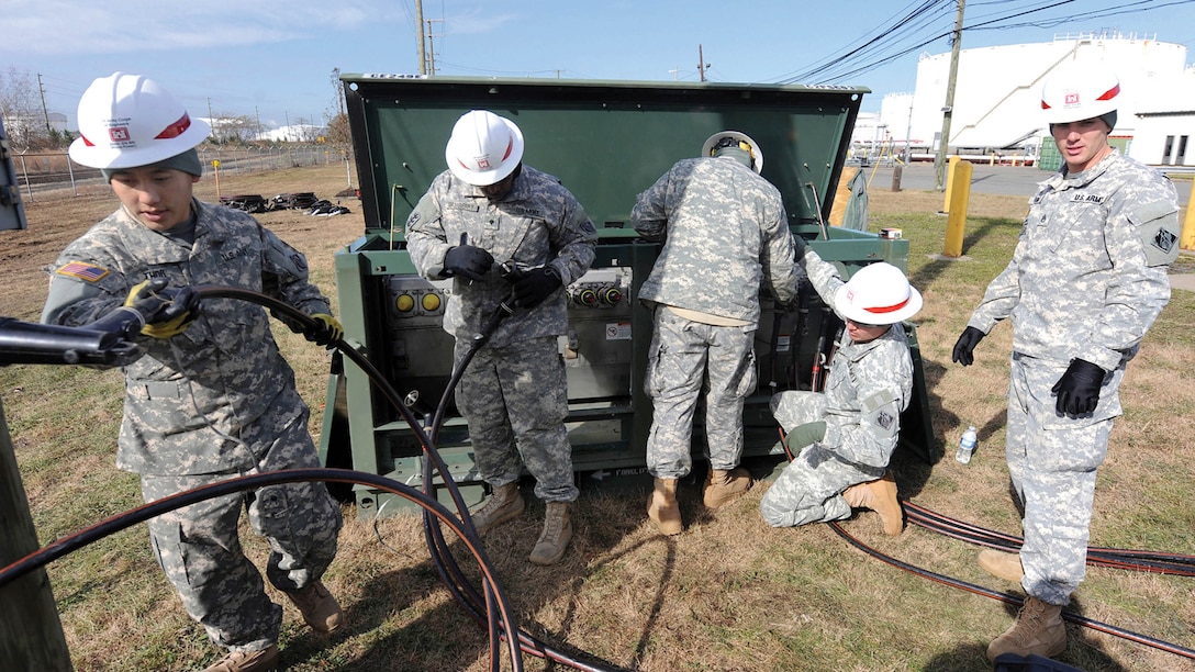 Soldiers in hardhats move a group of hoses.