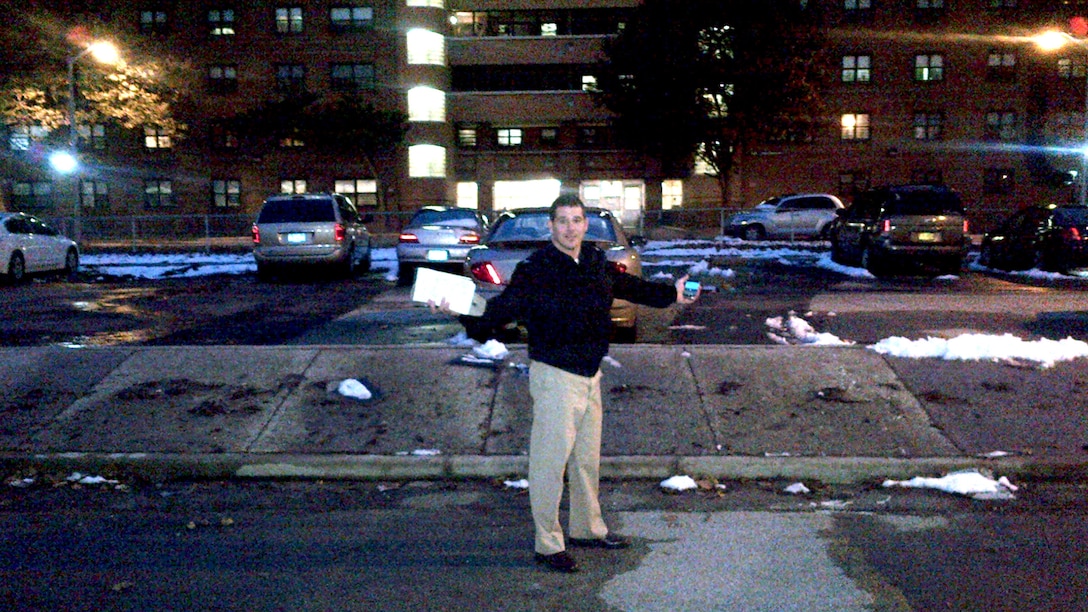 Man stands with his arms stretched out in front of a lit building during the night.