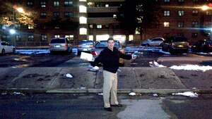 Man stands with his arms stretched out in front of a lit building during the night.