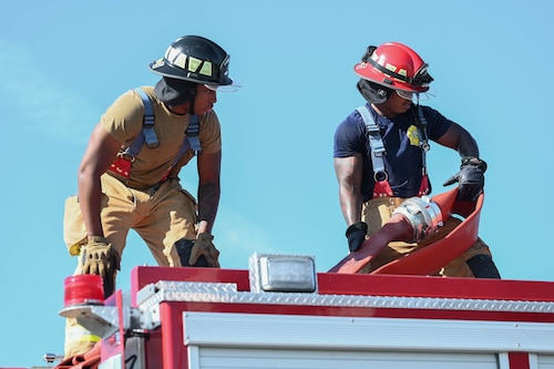 two firefighters stand on top of a fire truck