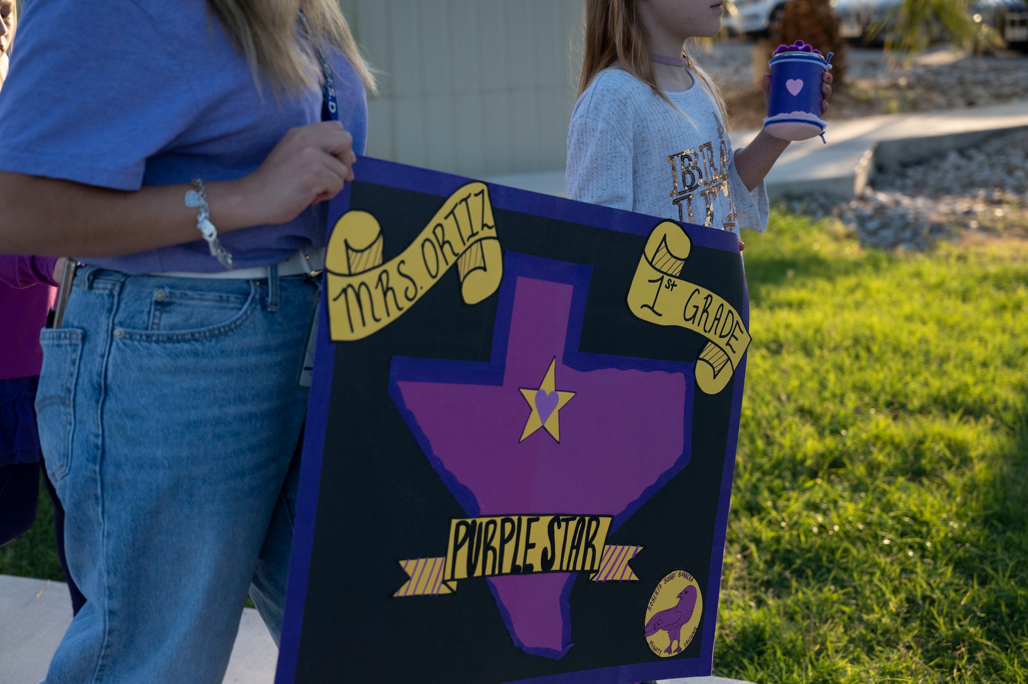 A staﬀ member and student from the Roberto Bobby Barrera (RBB) Elementary School hold up a sign during the “Purple Parade” held at Laughlin Air Force Base, Texas, Sept. 29, 2022. The “Purple Parade” was held in celebration of RBB Elementary School receiving the Purple Star Award, recognizing the support and commitment the school provides to meeting the unique needs of military-connected students and their families. (U.S. Air Force photo by Airman 1st Class Kailee Reynolds)