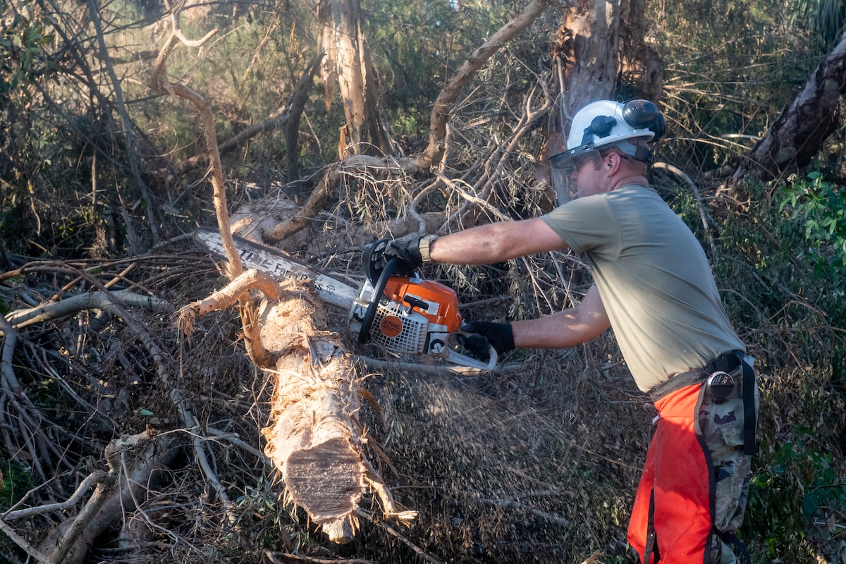 An Airman from the 202nd Rapid Engineer Deployable Heavy Operational Repair Squadron Engineers (RED HORSE) Squadron, Florida Air National Guard, cuts a tree blocking a road in St. James City, Pine Island, Fla. in response to Hurricane Ian, Oct. 4, 2022. The 202nd RED HORSE Squadron, stationed at Camp Blanding, Fla., is a specialized, highly mobile civil engineering team comprised of Florida Air National Guardsmen that provides rapid response capabilities for multiple worldwide contingencies and operations. (U.S. Air National Guard photo by Senior Airman Jacob Hancock)