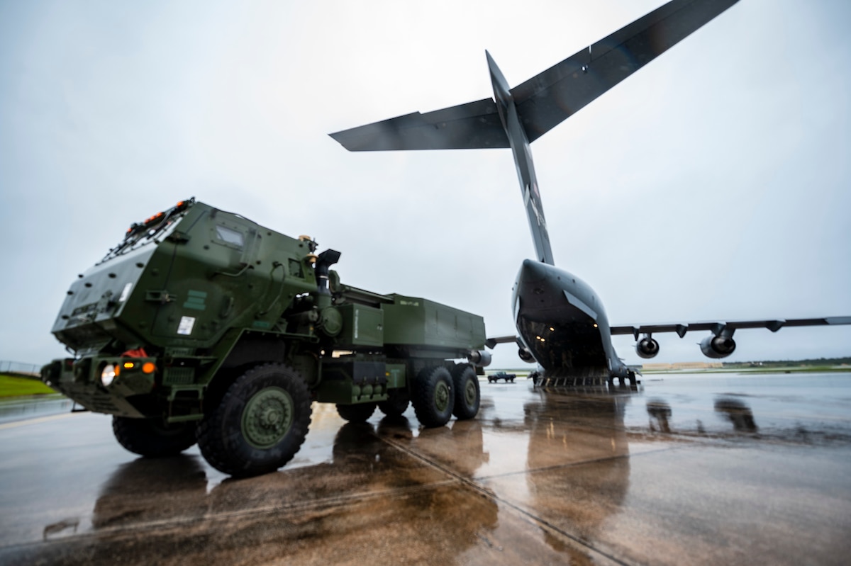 A military vehicle is parked near a plane