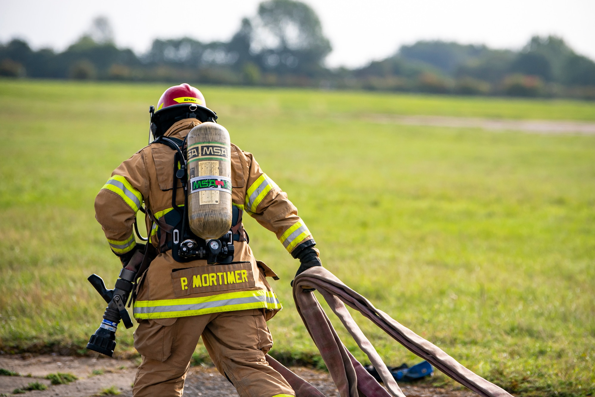 A firefighter from the  422d Fire Emergency Services, pulls a fire hose during a live-fire training exercise at RAF Fairford, England, Oct. 3, 2022. Firefighters from the 422d FES, are required to complete live-fire training bi-annualy to test thief overall readiness and ability to properly extinguish an aircraft fire. (U.S. Air Force photo by Staff Sgt. Eugene Oliver)