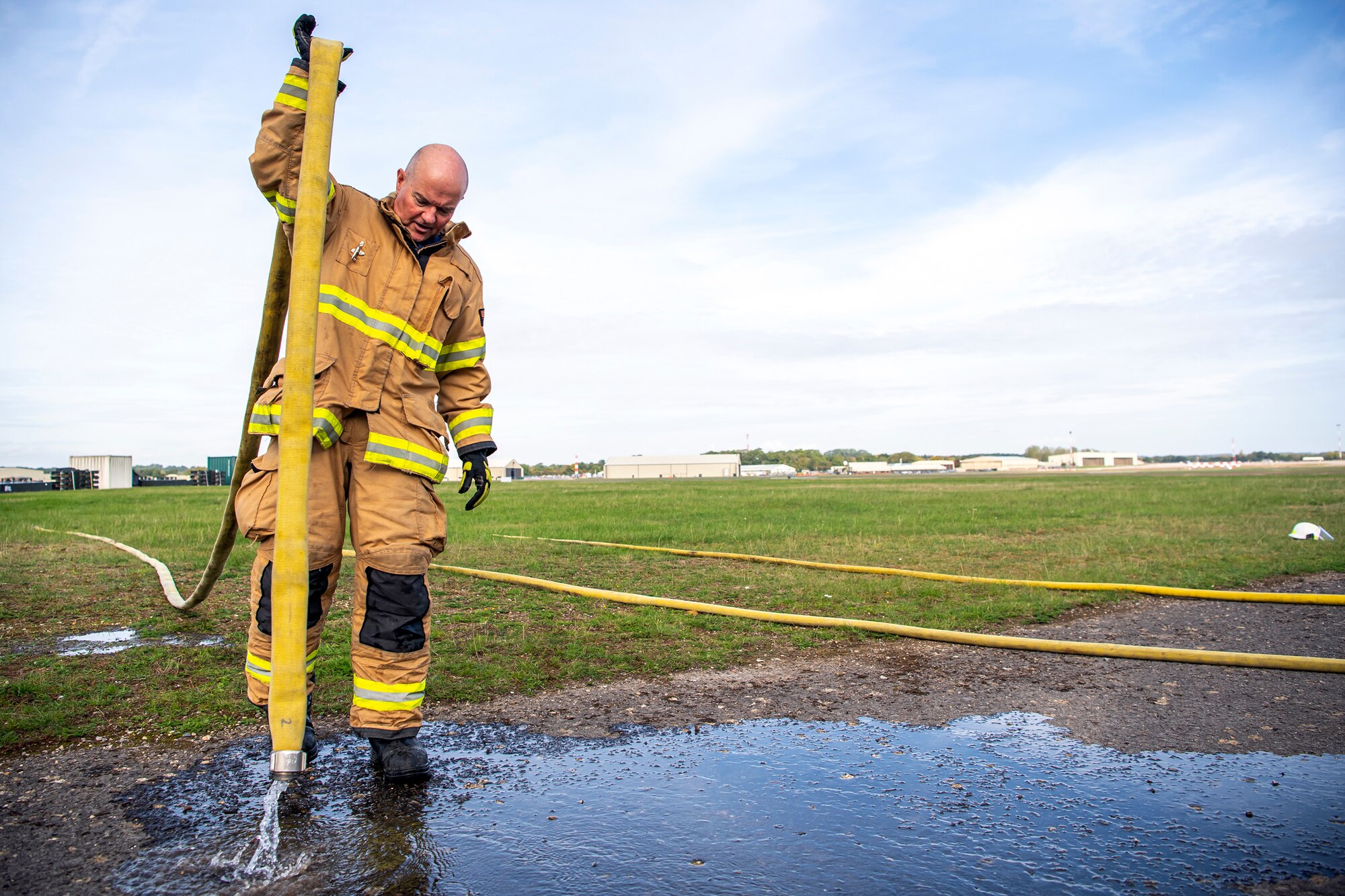 A firefighter from the 422d Fire Emergency Services empties a fire hose following a live-fire training exercise at RAF Fairford, England, Oct. 3, 2022. Firefighters from the 422d FES, are required to complete live-fire training bi-annualy to test thief overall readiness and ability to properly extinguish an aircraft fire. (U.S. Air Force photo by Staff Sgt. Eugene Oliver)