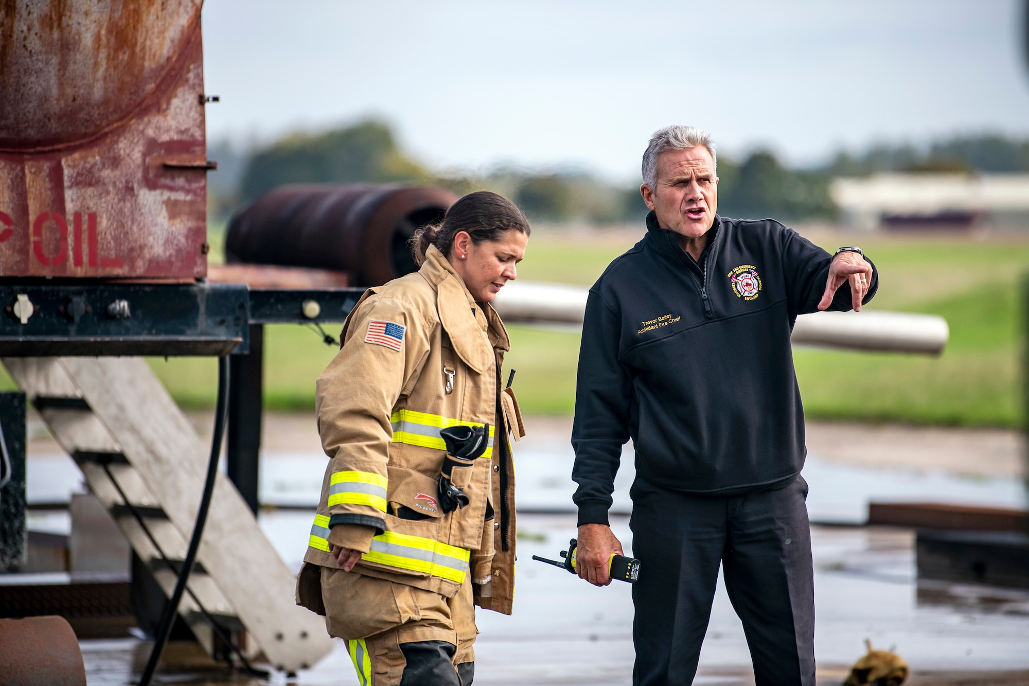 A firefighter from the 422d Fire Emergency Services speaks with Trevor Bailey, 422d FES assistant fire chief, following a live-fire training exercise at RAF Fairford, England, Oct. 3, 2022. Firefighters from the 422d FES, are required to complete live-fire training bi-annualy to test thief overall readiness and ability to properly extinguish an aircraft fire. (U.S. Air Force photo by Staff Sgt. Eugene Oliver)