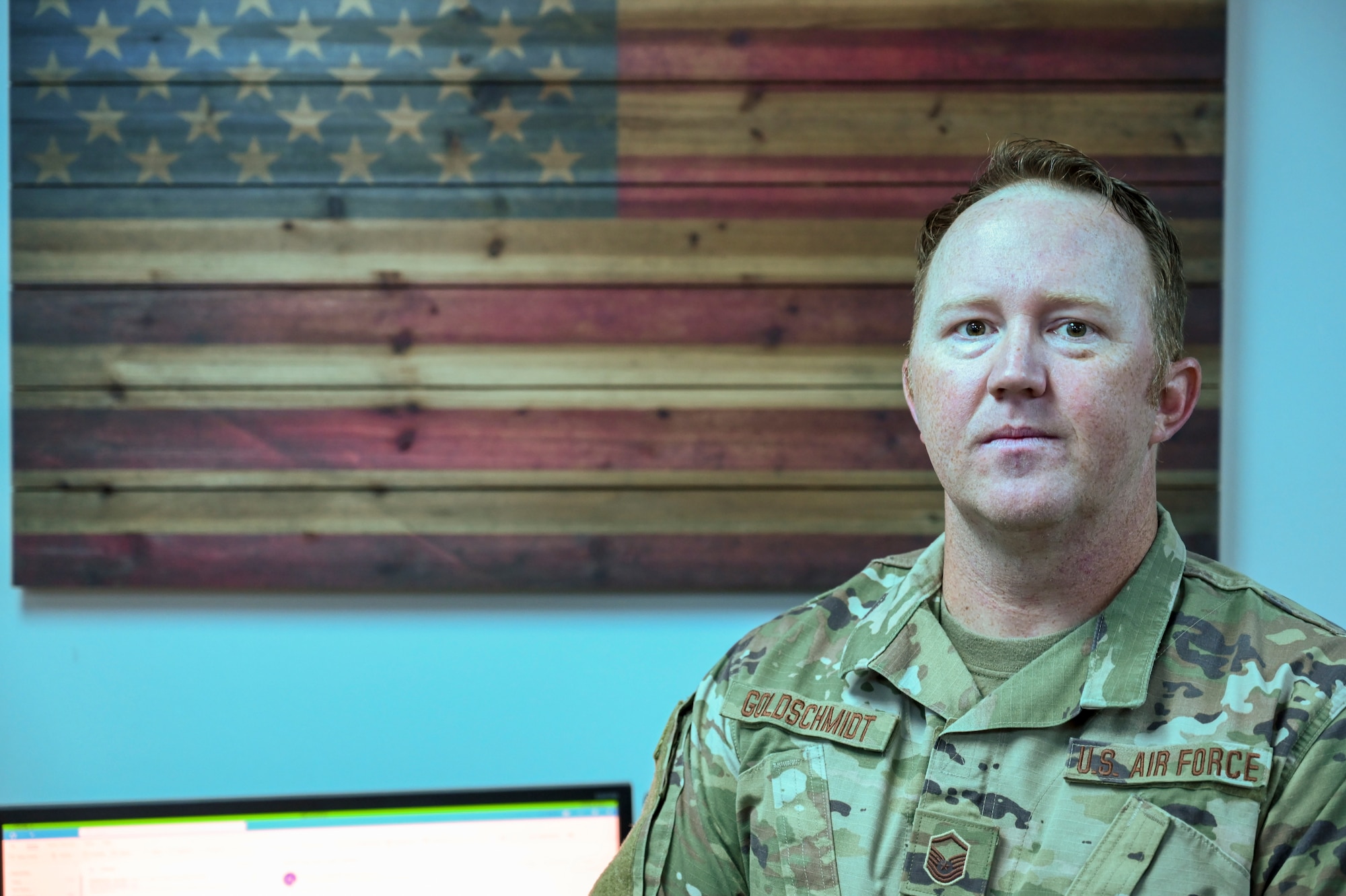 A man poses for a picture in front of a wooden American Flag