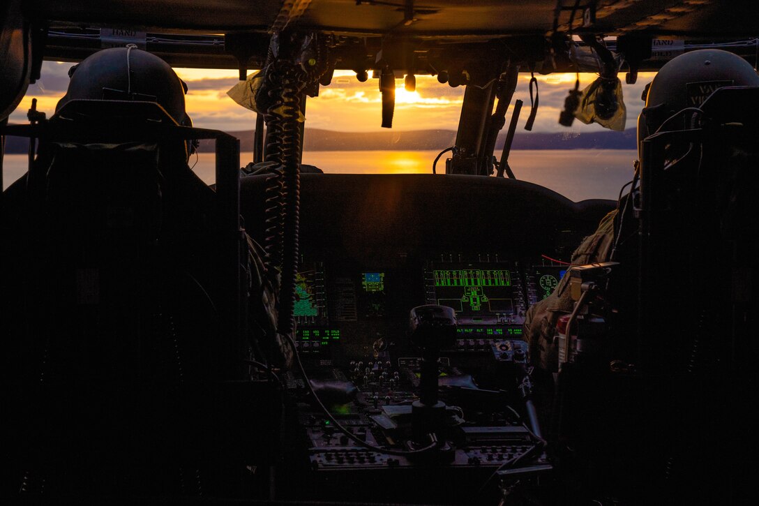 Two pilots sit in a cockpit as they fly over water at twilight.