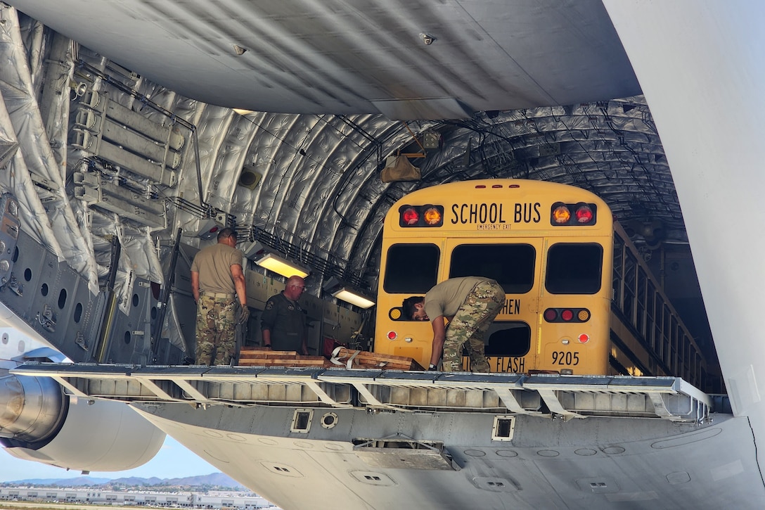 Airmen load a school bus into the back of an aircraft.