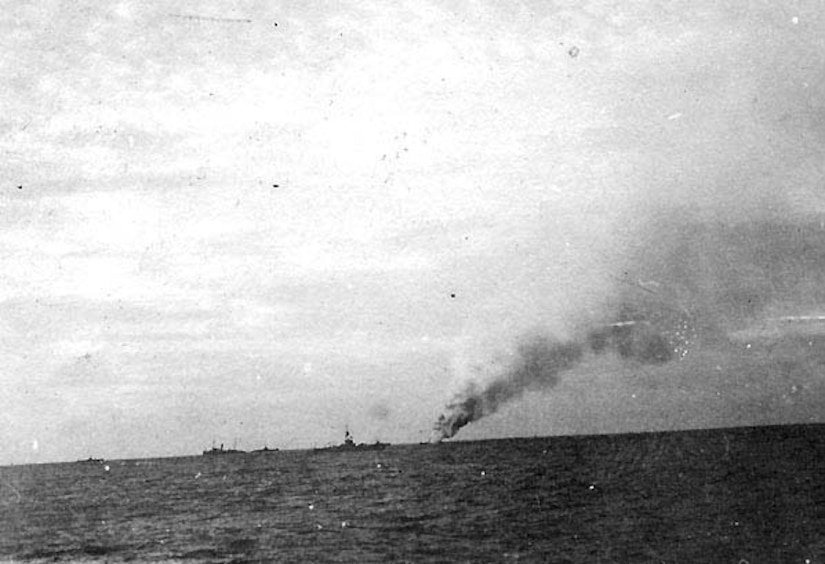 Smoke emanates from a small ship as a larger ship sits nearby.