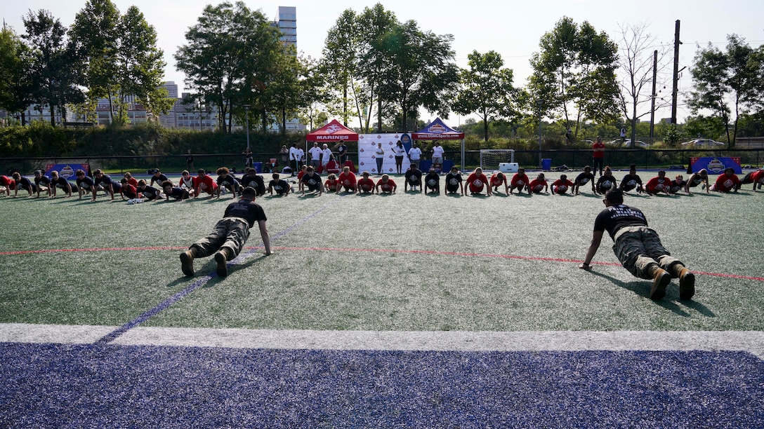 U.S. Marine Corps Staff Sgt. Antonio Tellez, left, and Staff Sgt. Philip Deocampo, canvassing recruiters with Recruiting Station Harrisburg, lead lacrosse players in push-ups during a Sports Leadership Academy lacrosse clinic in Philadelphia, Pennsylvania, Sep. 17, 2022.