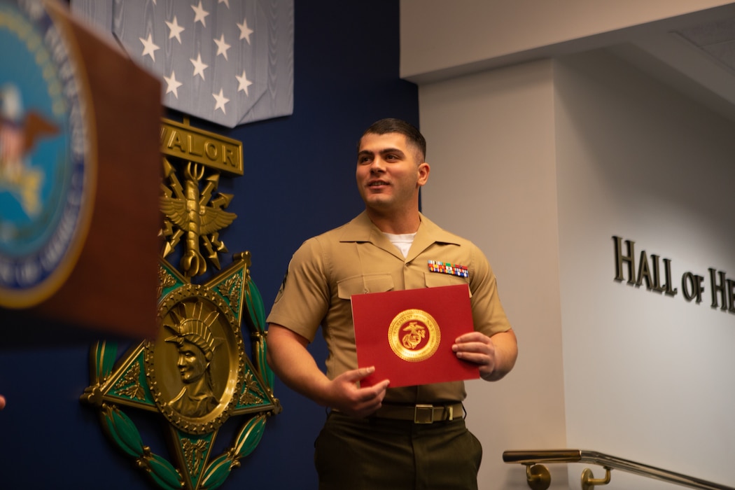 A Marine speaking while holding a red award.