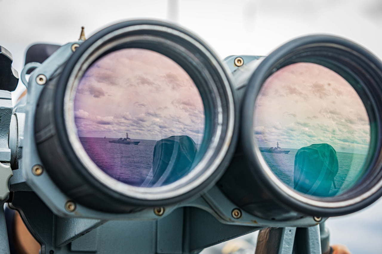 A pair of binoculars displays a reflection of two ships at sea.
