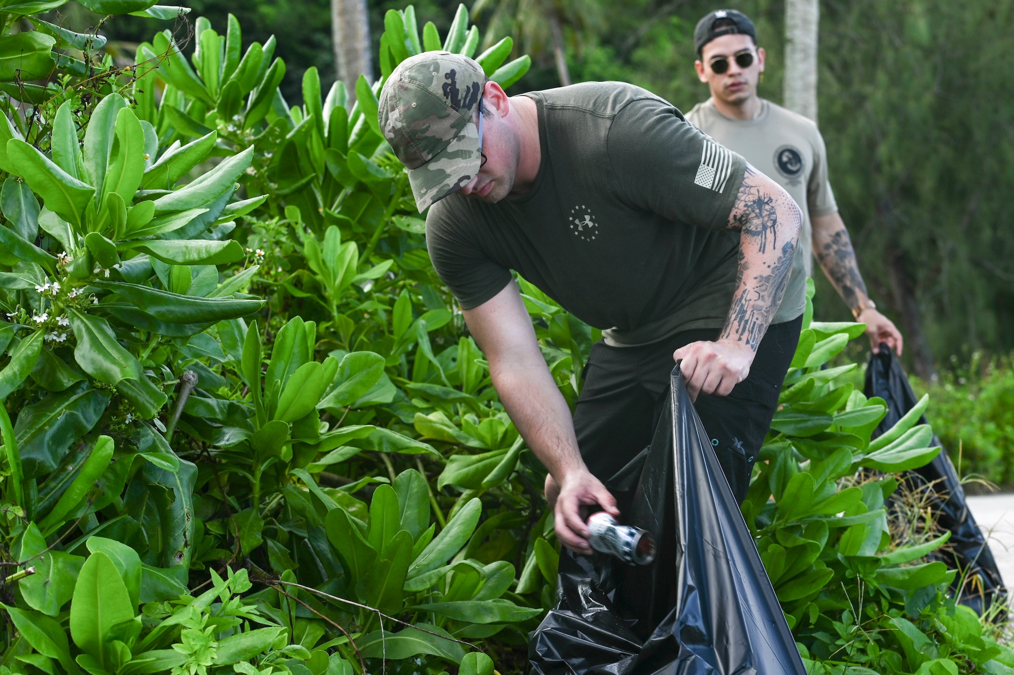 Airman picking up a can and placing it in a trash bad.