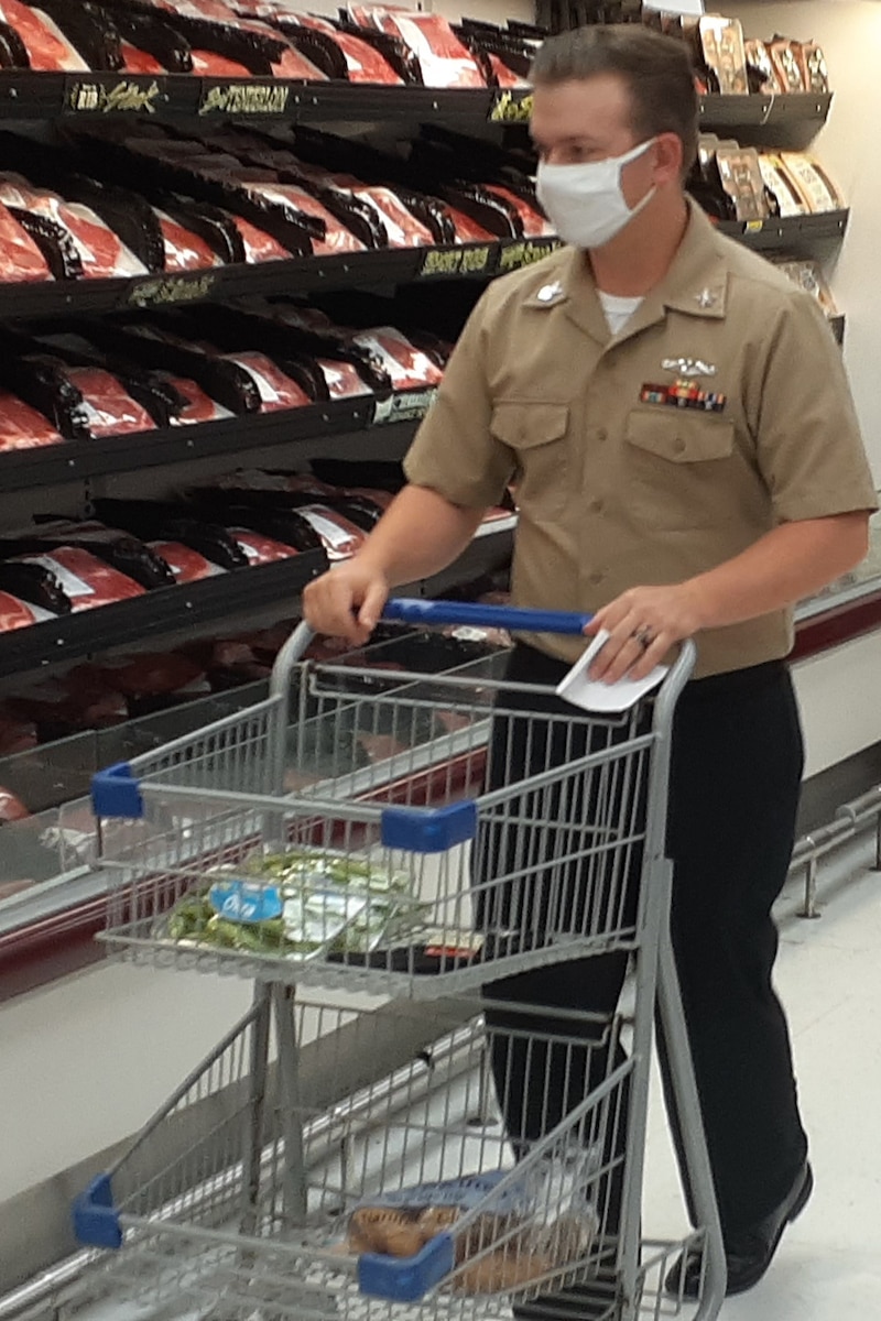A man in uniform pushes a grocery cart past packaged meats.