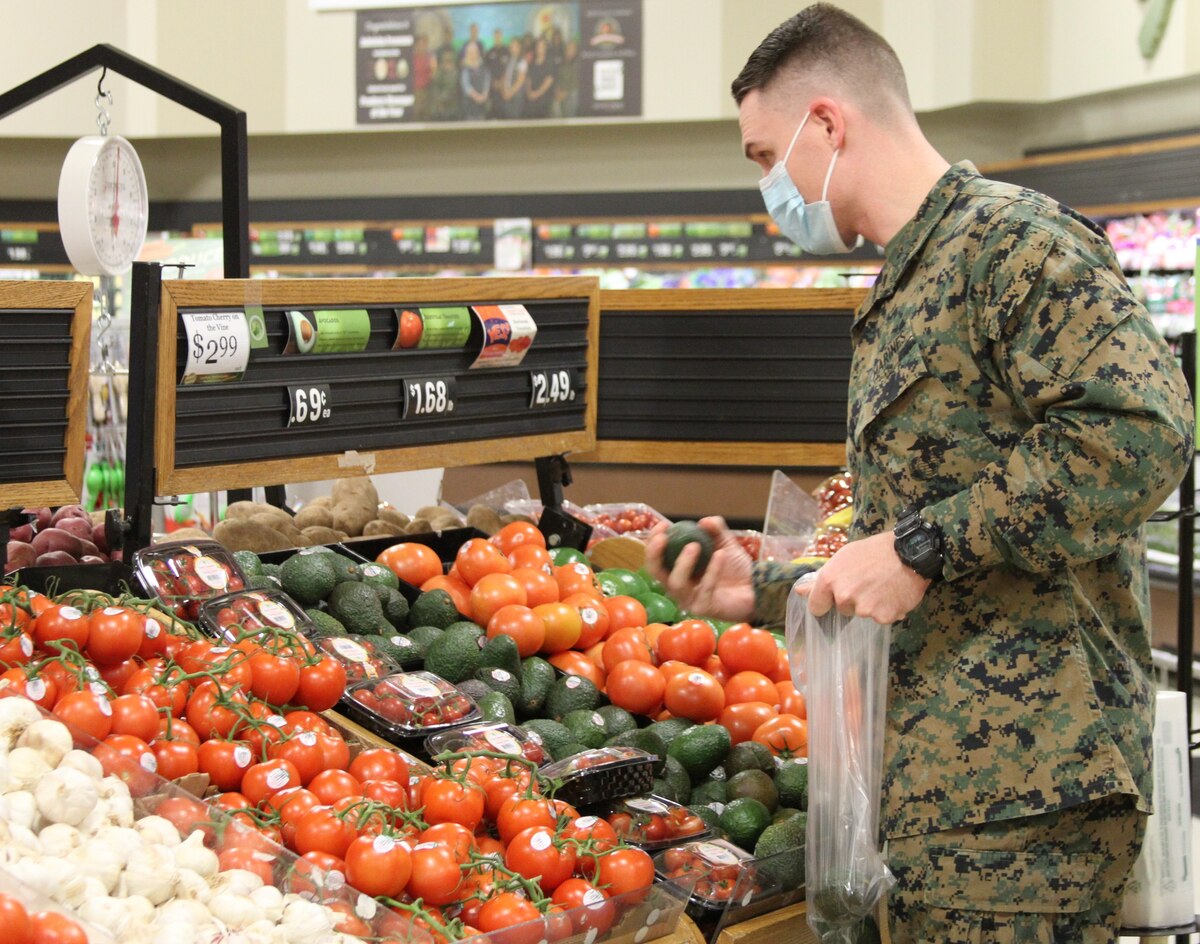 A uniformed service member has a plastic bag in one hand and looks at a produce display.
