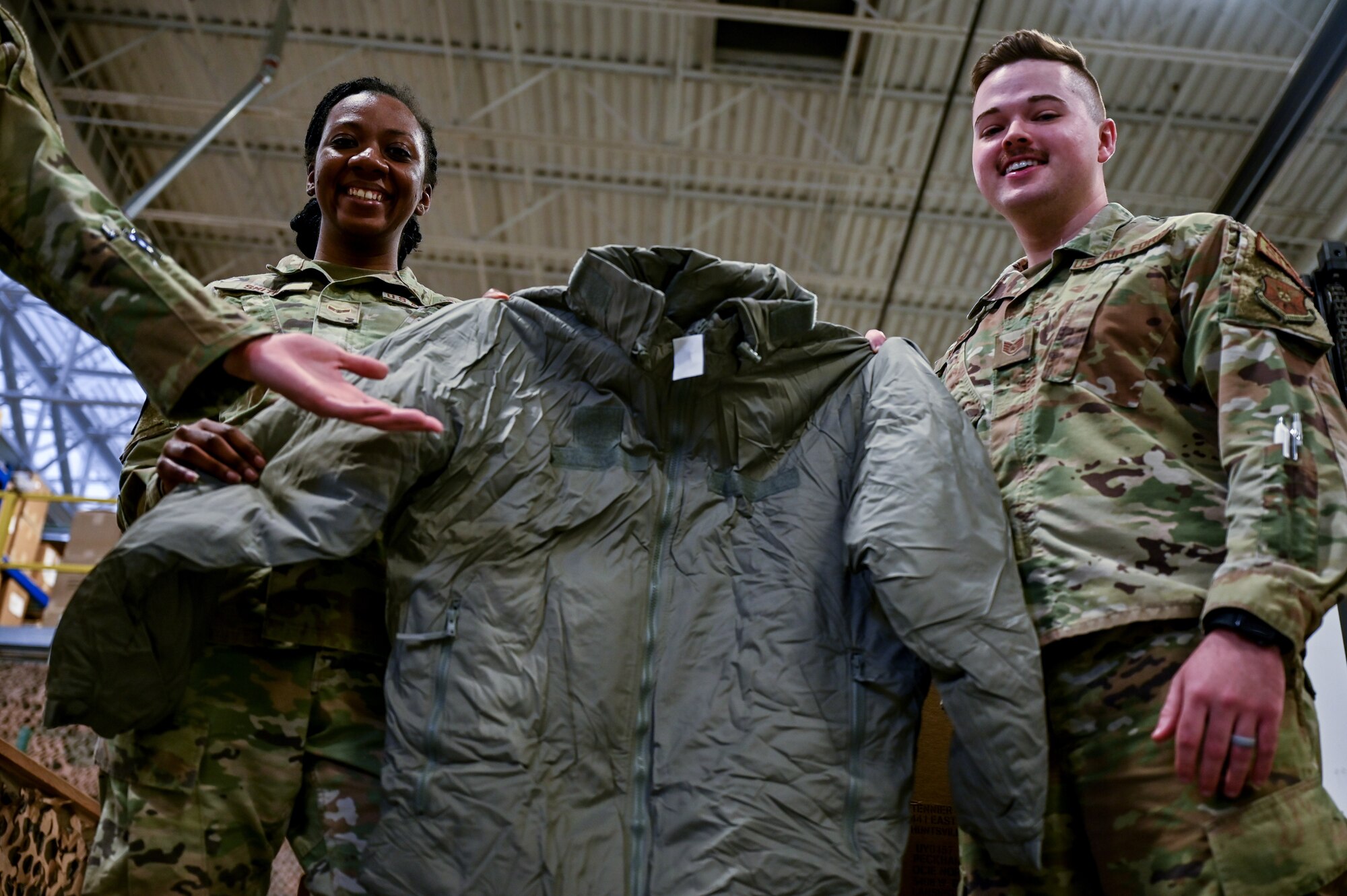 Airman 1st Class Destiny Smith, 90th Logistics Readiness Squadron mobility journeyman, and Staff Sgt. Jacob Wilson, 90 LRS mobility NCOIC, hold a parka to show what they packed on F.E. Warren Air Force Base, Wyoming, Sept. 29, 2022. As part of a Department of Defense effort to provide foreign aid, the 90 LRS mobility flight packed and shipped 111 parkas to the front lines in Eastern Europe. (U.S. Air Force photo by Joseph Coslett)