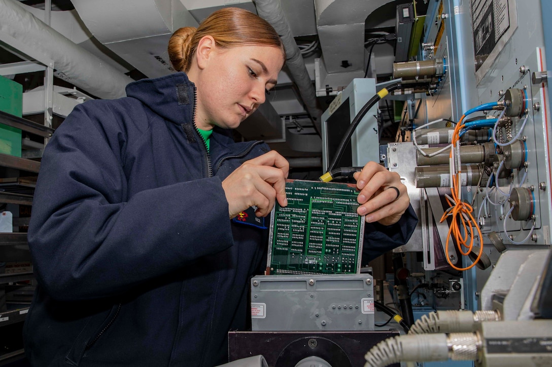 A sailor places a circuit board into a machine.