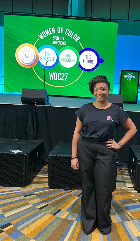 women standing in front of a stage with a green display with a women of color logo.