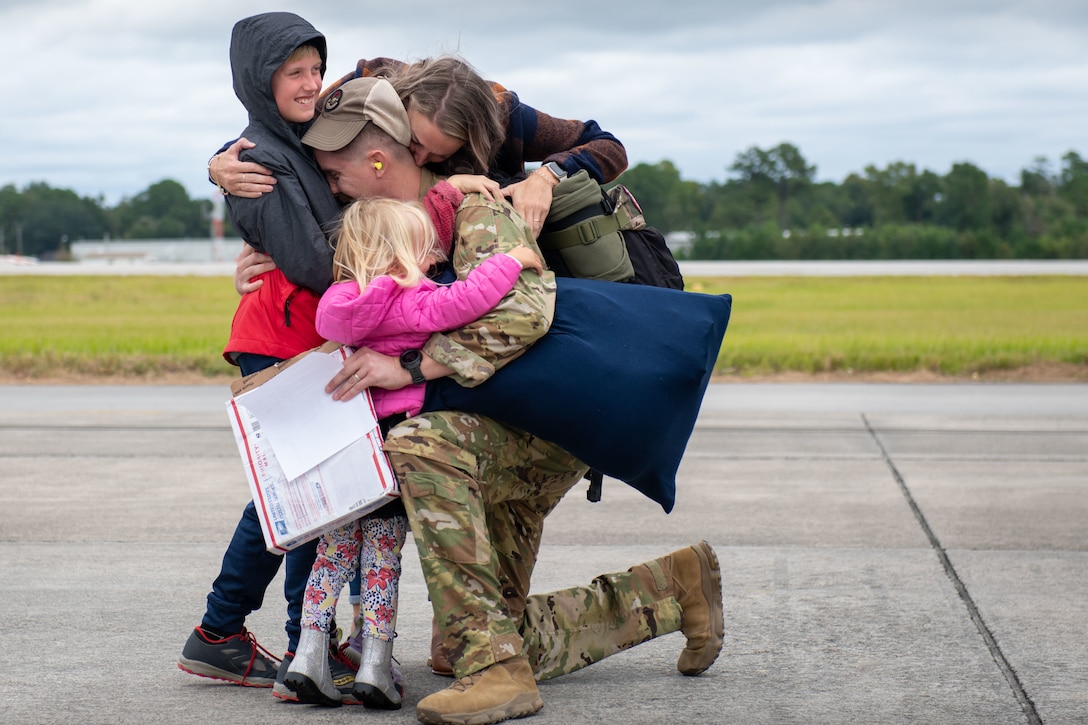 An airman kneels on pavement while sharing an embrace with three family members.