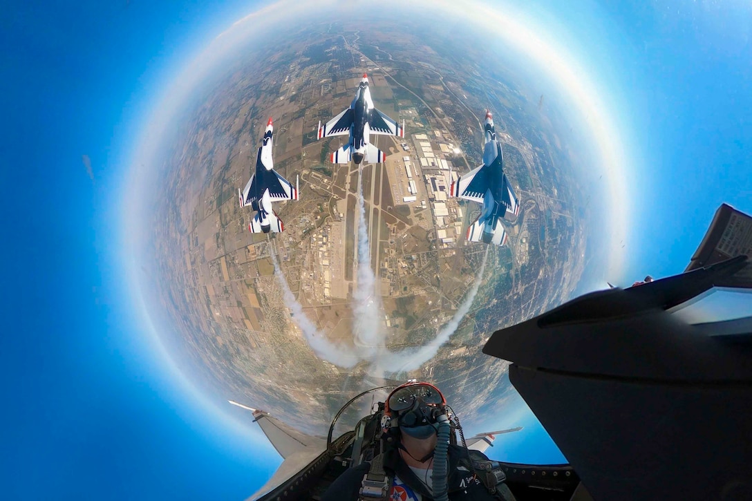 A look from inside a cockpit at an airman in midair as three other aircraft fly below.