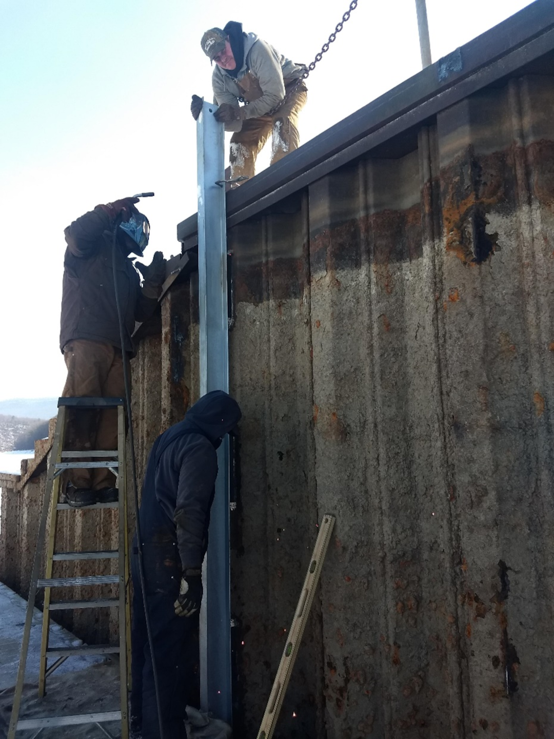 Work crews are at work replacing steel I-beams at James Creek during the 2021 drawdown of Raystown Lake. One man stands on the top of the structure, while another works from a ladder and a third stands on the ground.