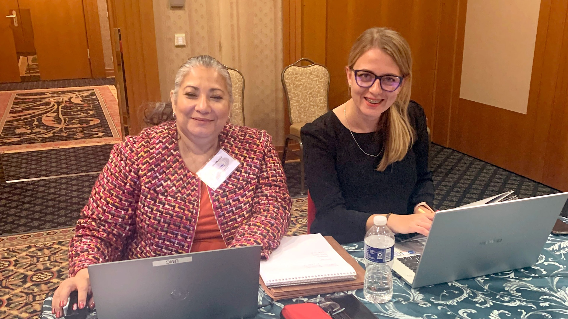 two women sit next to one another with computers
