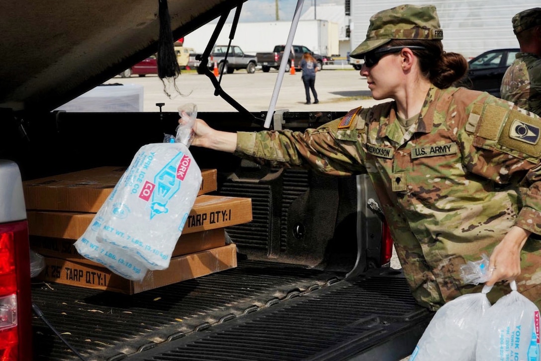 A soldier put bags of ice into the back of a vehicle.