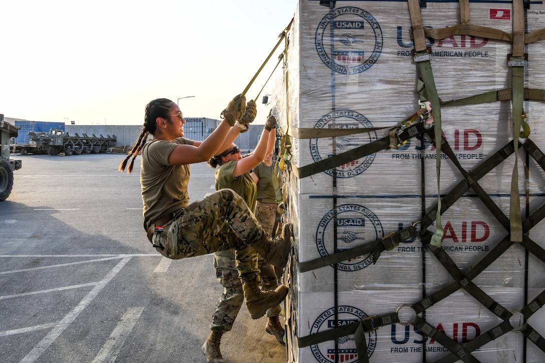 A soldier uses her body weight to secure supplies to a pallet.