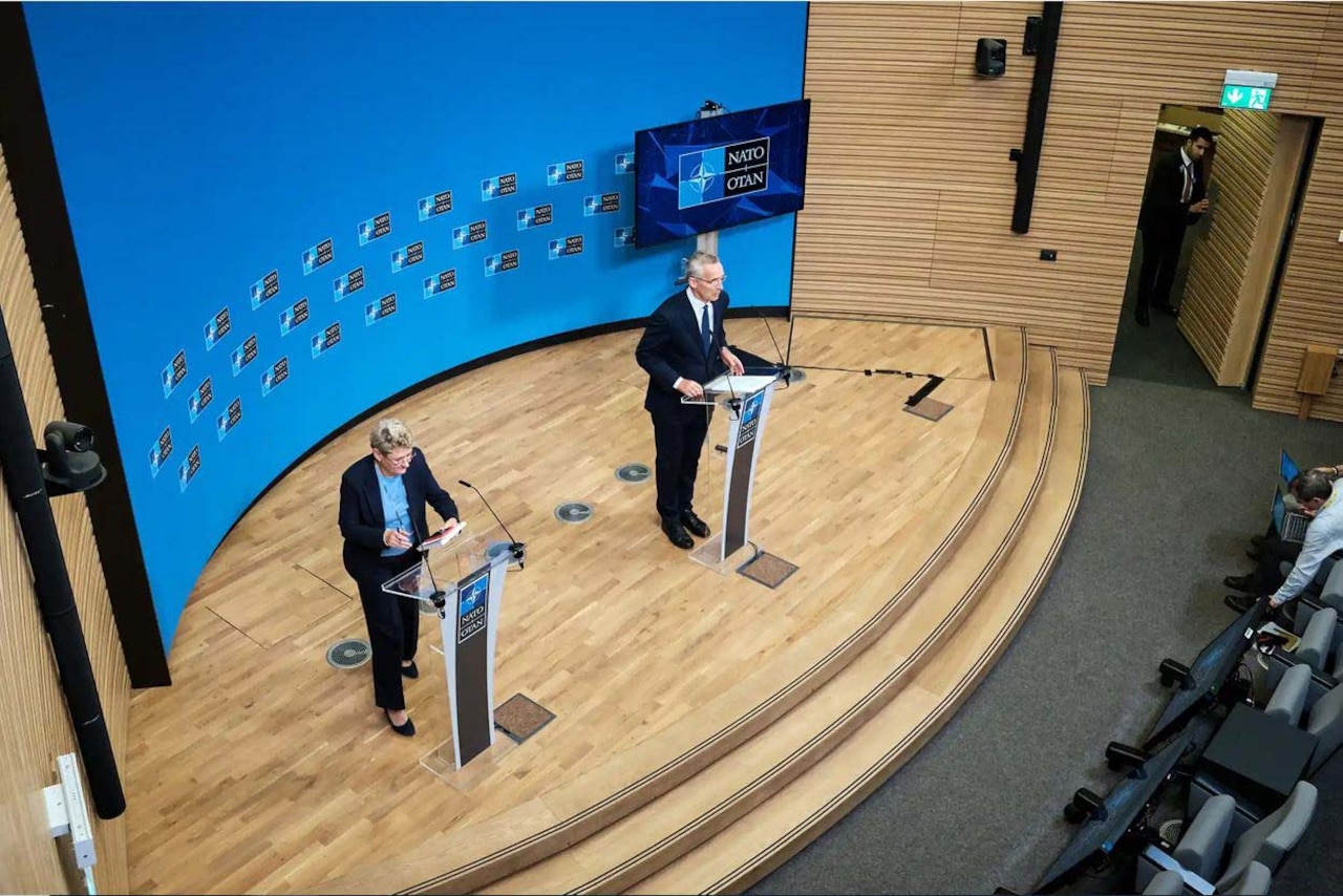 A news conference, as viewed from above, shows two people standing at lecterns.