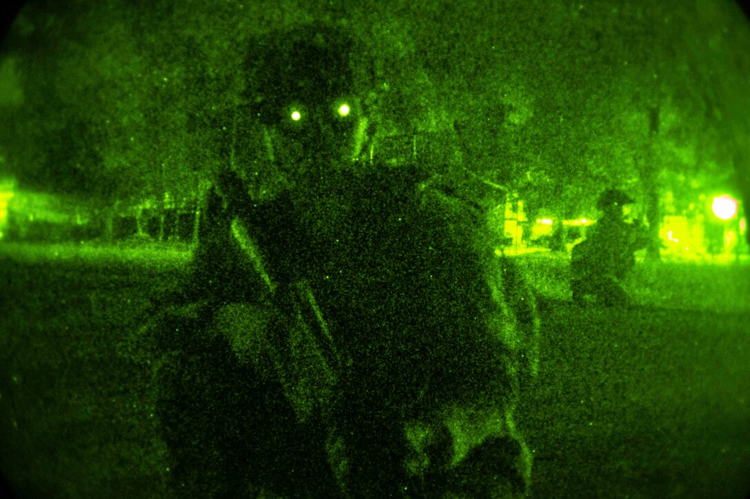 U.S. and Philippine marines wearing night vision goggles hold weapons while kneeling on the ground.
