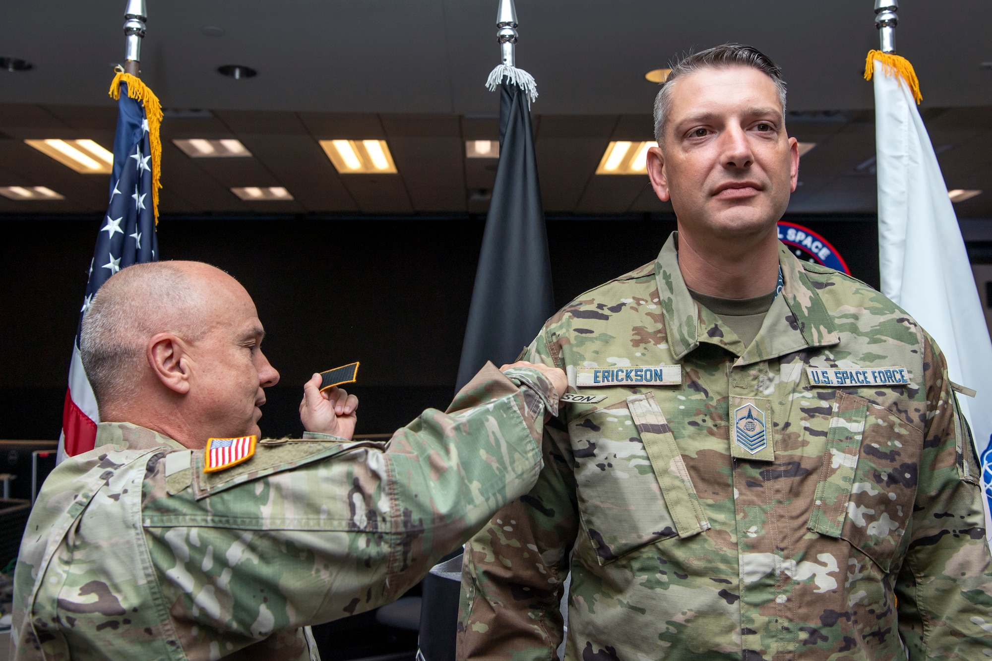 Man in military uniform places new patches on another man in military uniform