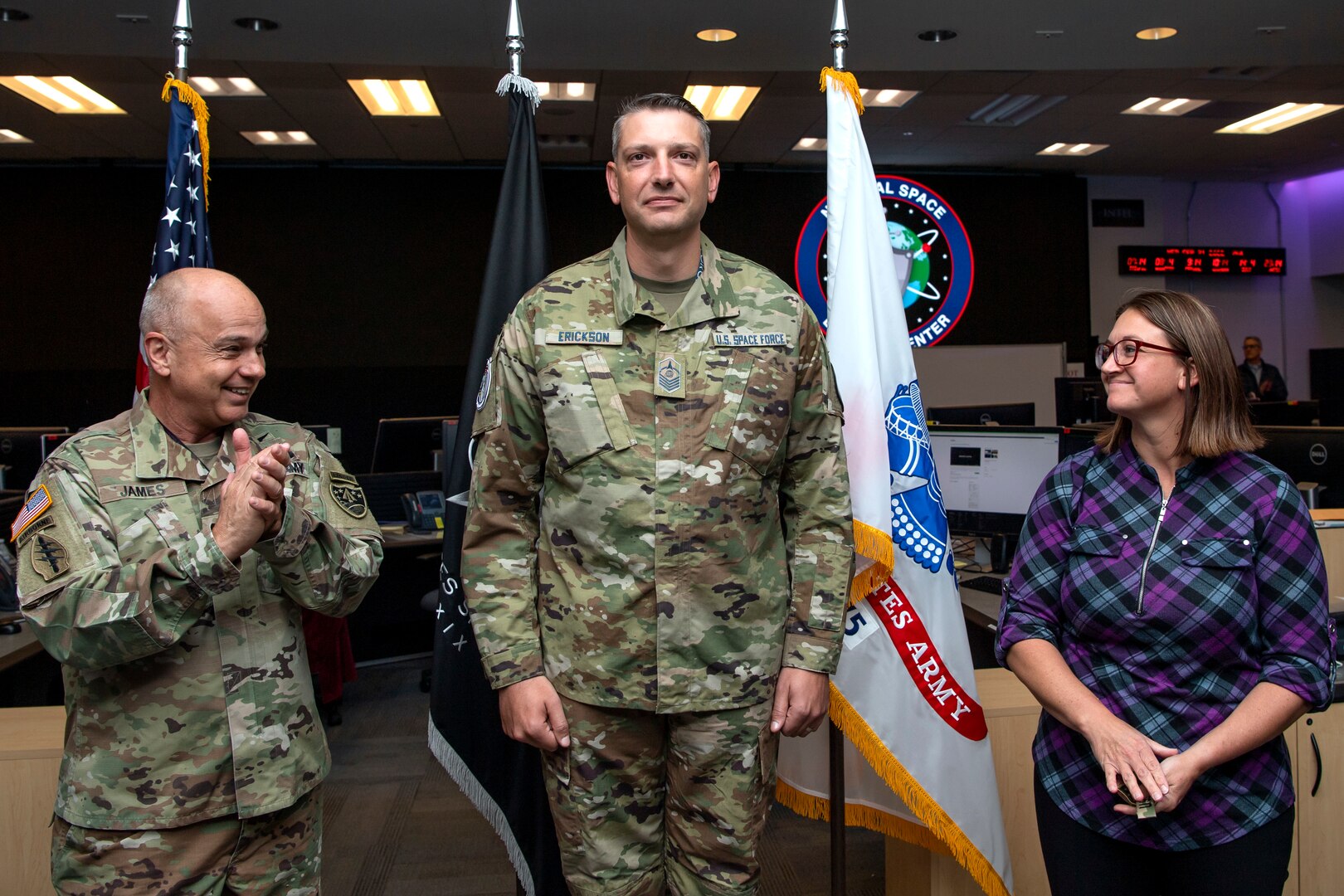 A man in military uniform and woman in plaid take patches off another man in military uniform