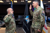 Two military men in uniform hold up their right hands to recite the oath of enlistment during a ceremony