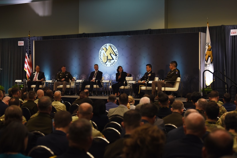 A six-person panel sits on a stage in front of a crowd of people.