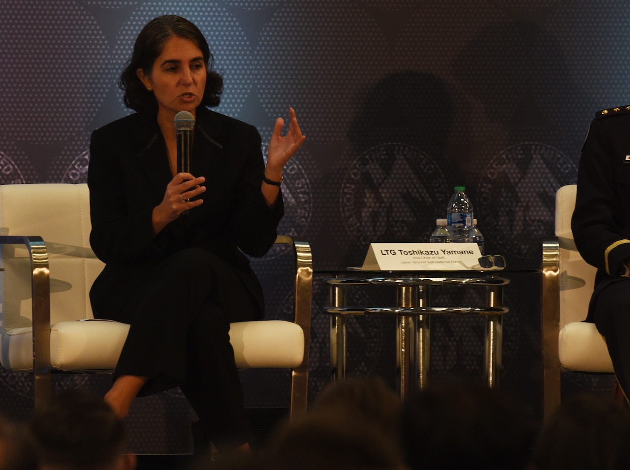 A woman sits in a chair and speaks into a microphone.