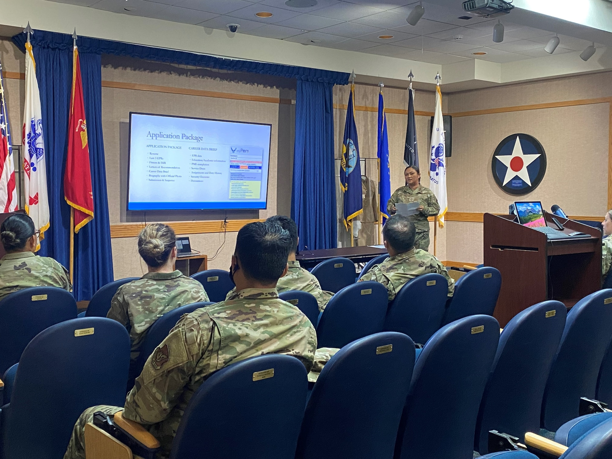 Senior enlisted Airmen stand at front of auditorium addressing audience of junior enlisted Airmen.