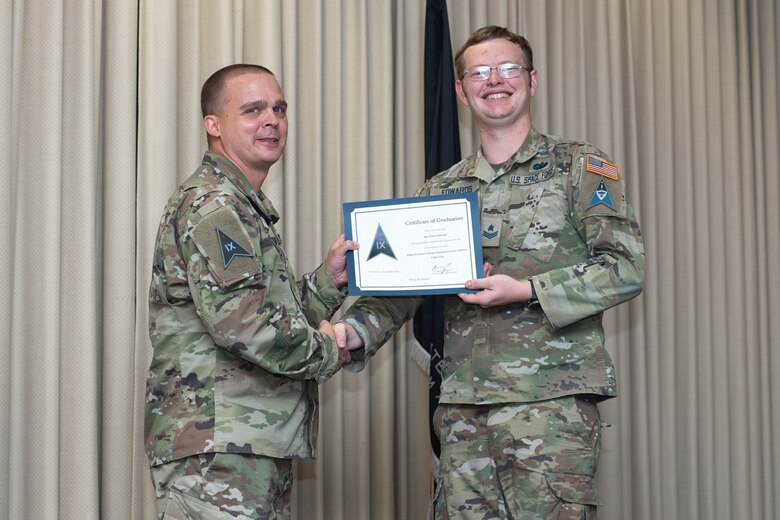 U.S. Space Force Col. Mark Bigley, Space Delta 9 commander, presents a graduation certificate to Sgt. Dylan Edwards.