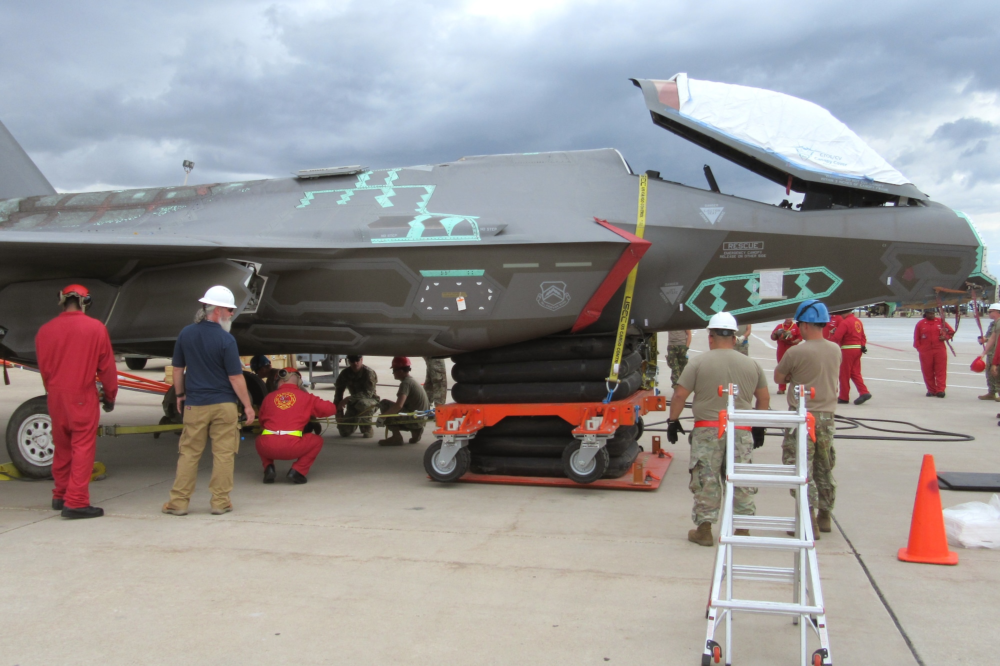 Students doing various tasks around a reassembled F-35 with its nose sitting on airbags.