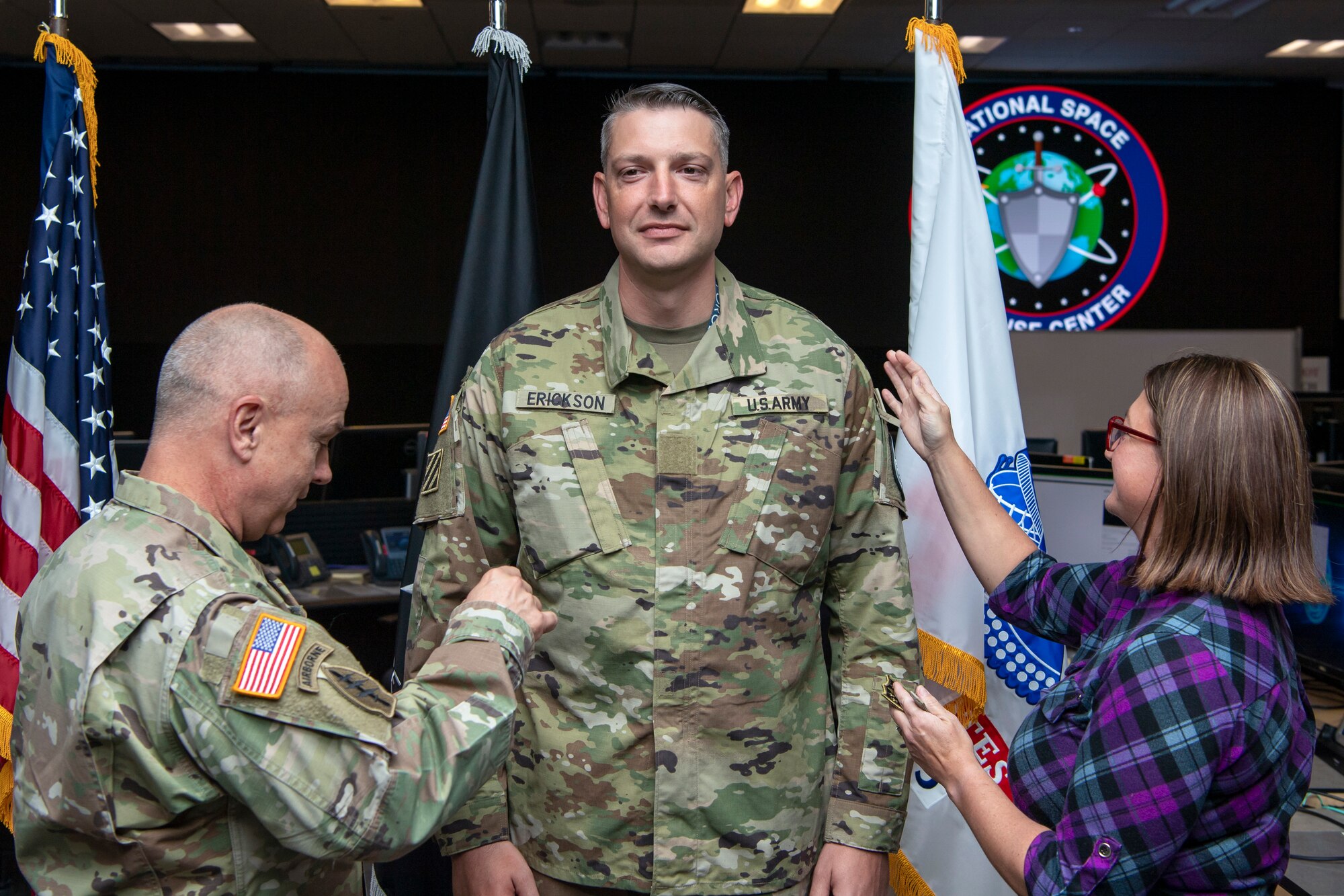 Man in military uniform and woman in plaid take off patches from another man in military uniform