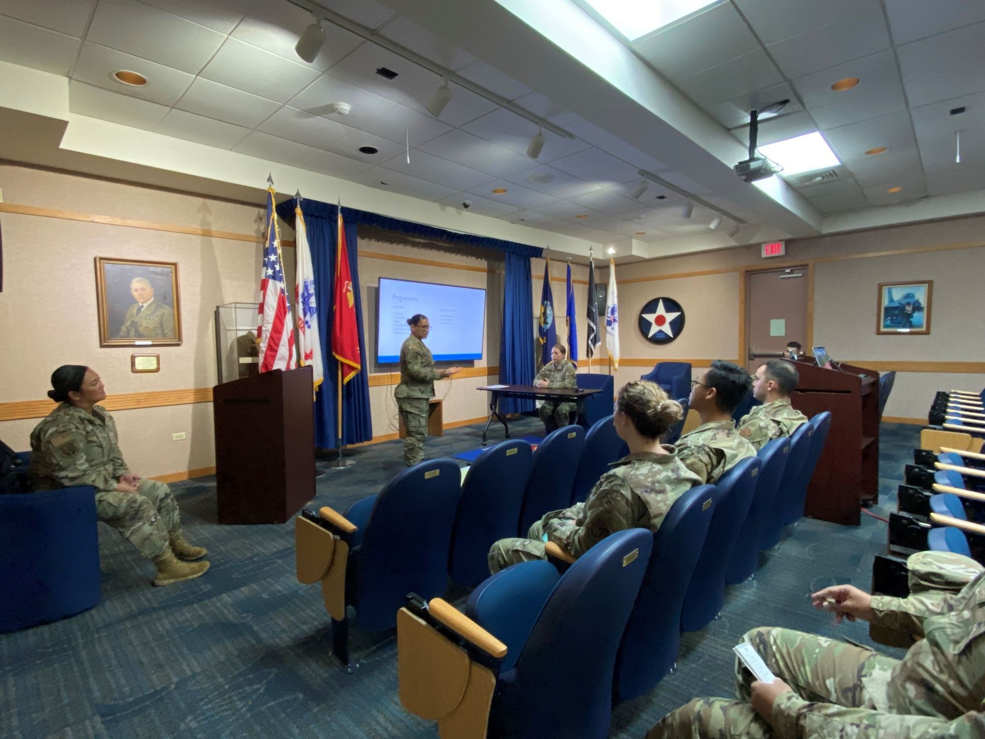 Senior enlisted Airmen stand at front of auditorium addressing audience of junior enlisted Airmen.