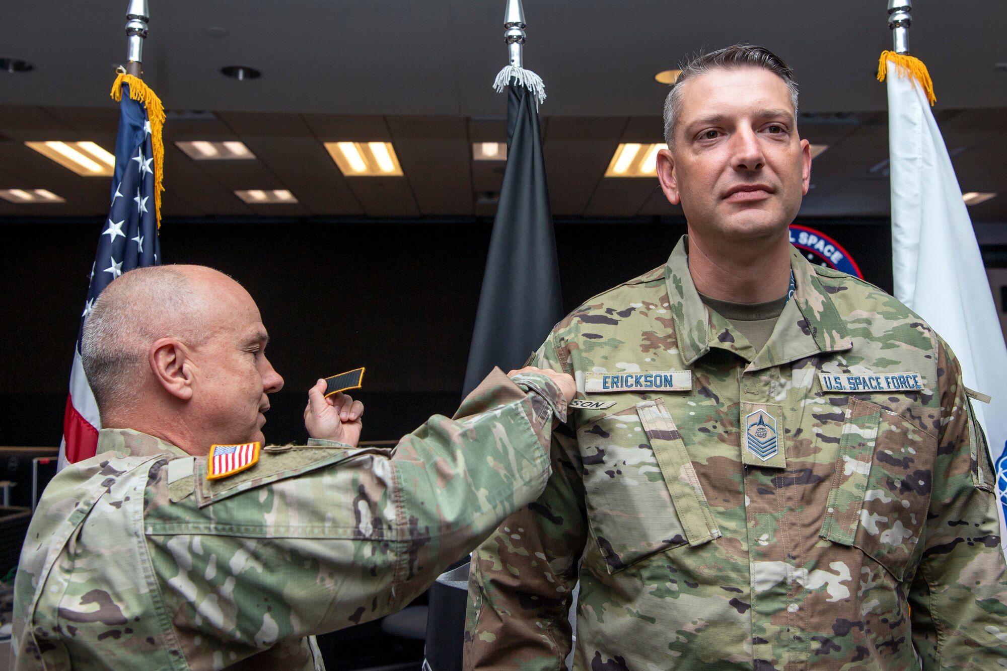 Man in military uniform places new patches on another man in military uniform
