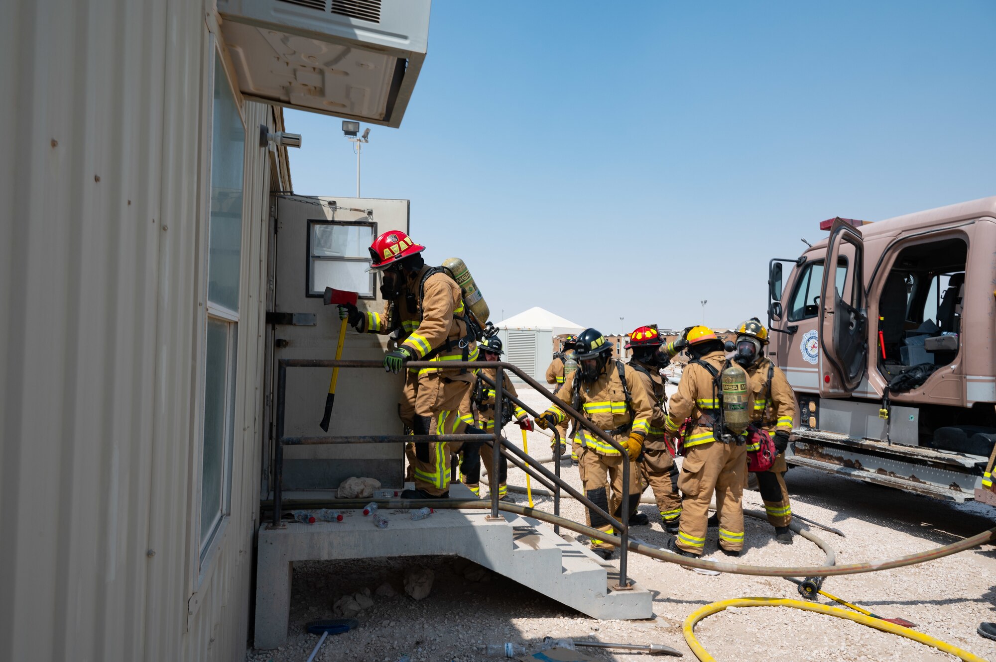 U.S. Air Force firefighters assigned to the 1st Expeditionary Civil Engineer Group, 577th Expeditionary Prime Beef Squadron, Quick Strike Team Fire enter a simulated hazardous environment during an exercise Aug. 30, 2022 at Al Udeid Air Base, Qatar. The firefighters practiced forcible entry techniques to enter a simulated immediate Danger to Life and Health environment to search for potential victims during an exercise. (U.S. Air Force photo by Staff Sgt. Dana Tourtellotte)
