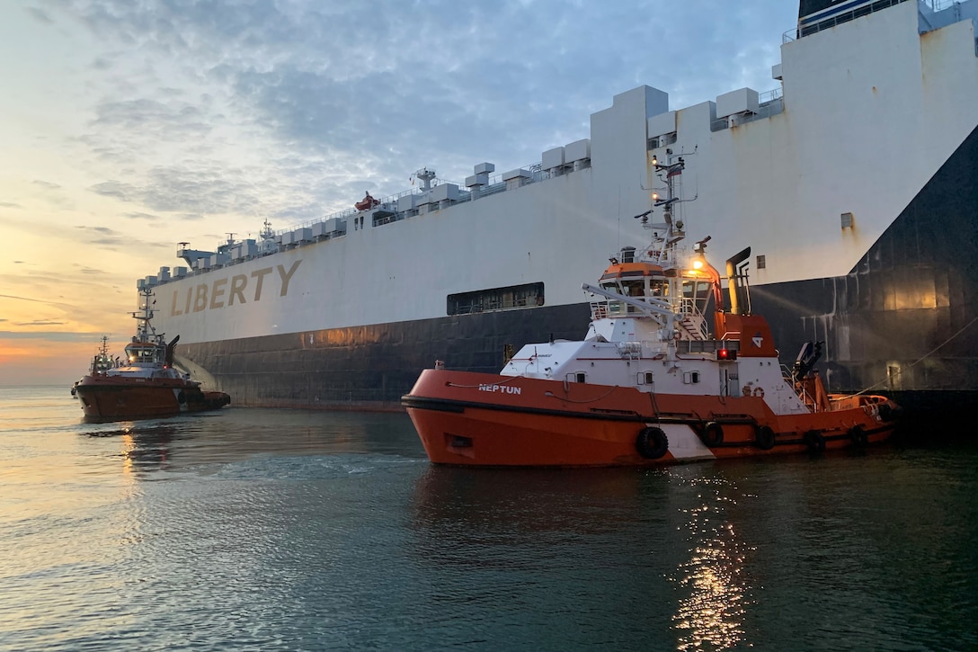 Two small boats float alongside a large cargo vessel.