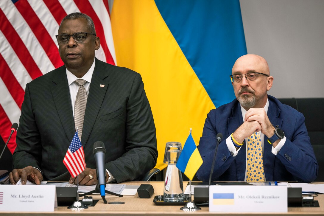 Two men look forward from behind a table.