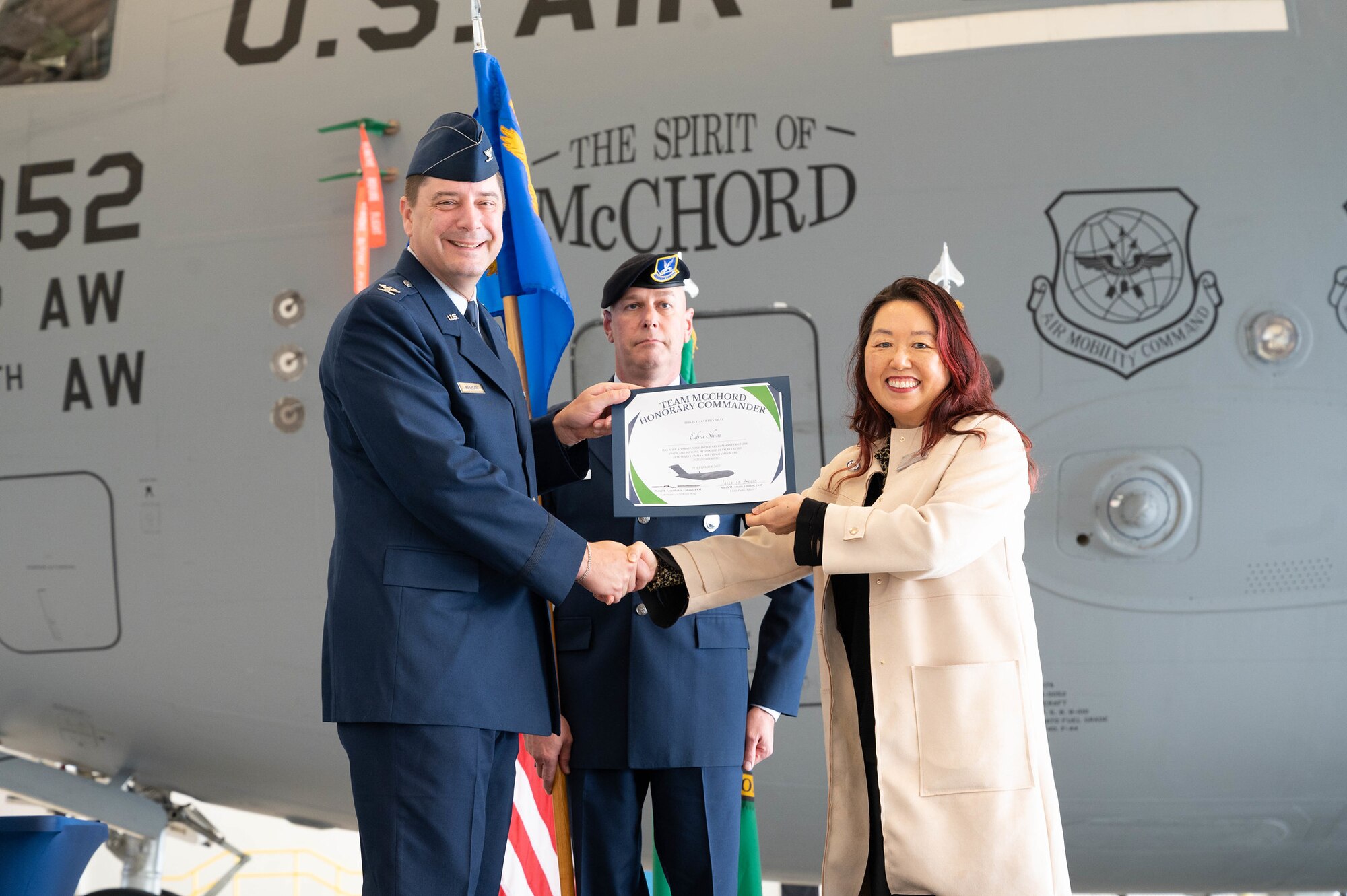Col. Charles Metzgar, U.S. Air Force, presents Edna Shim, Seattle Children's Hospital, with a certificate in front of a C-17 Globemaster III during the 2022 Honorary Commander Assumption of Command Ceremony at Joint Base Lewis-McChord.