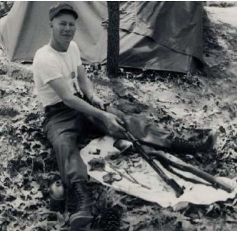 A man sitting on the ground cleans a rifle.