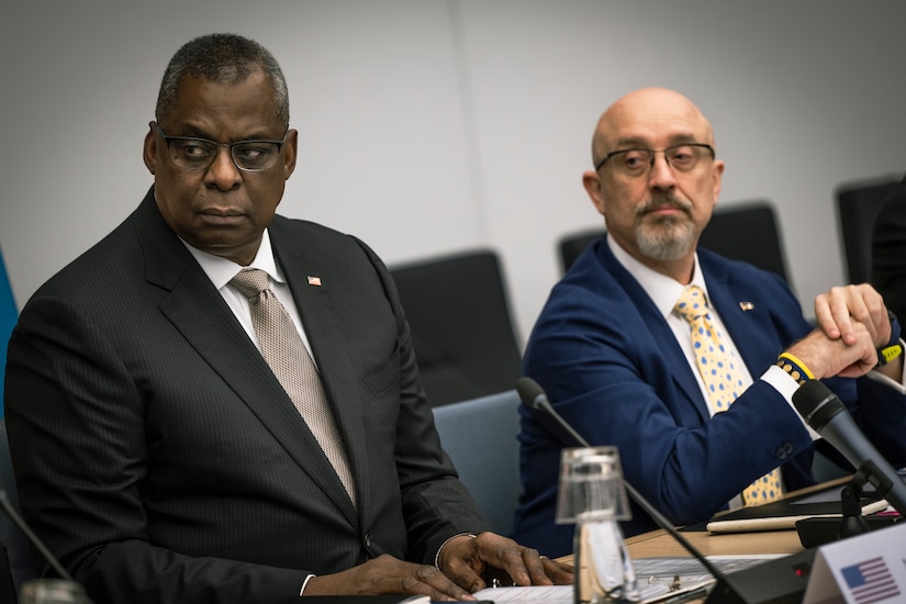 Two men sit at a table with microphones.